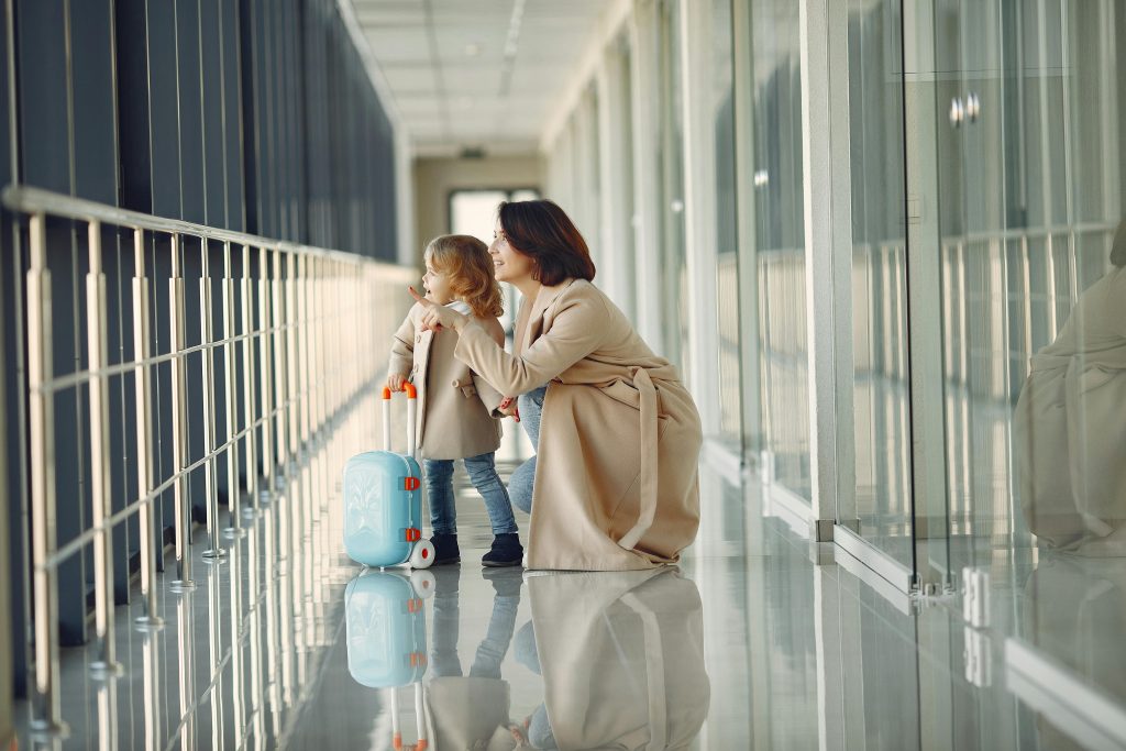 Uśmiechnięta mama z dzieckiem i walizkami na lotnisku, planująca legalny powrót do Polski i relokację po rozwodzie w Anglii.