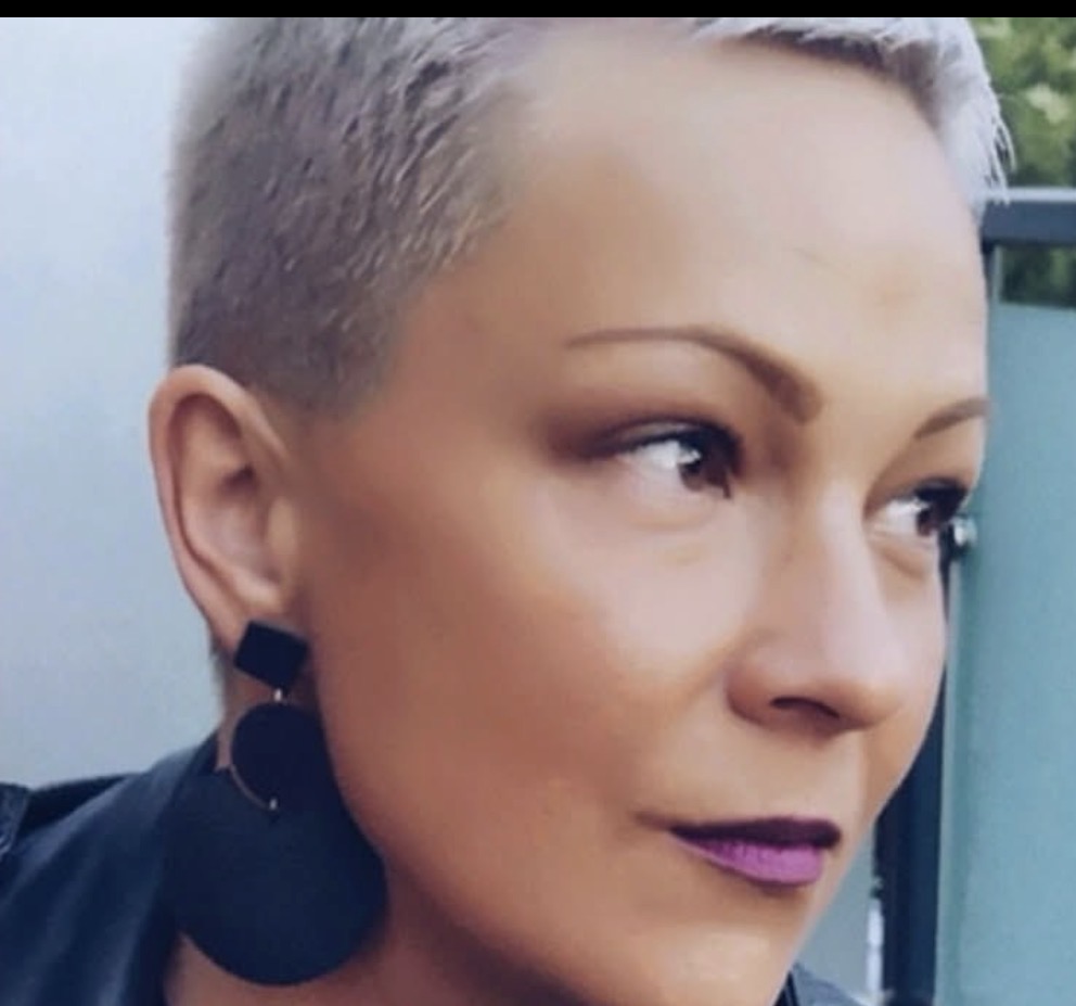Zadowoona klientka kancelarii Ask Montgomery Advocates, krótkie blond włosy, kolczyki i usta pomalowane bordową pomadką.